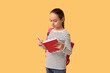© Pixel-Shot - Little schoolgirl reading book on yellow background