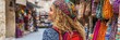 © Ilja - Young woman with curly hair exploring a vibrant authentic travel market with colorful handicrafts.