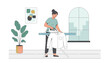 © EmilyGrace - Young woman standing in a cozy living room and ironing a fresh white shirt on an ironing board next to a houseplant.