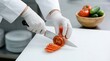 © SUHEB - A chef wearing white uniform and gloves slicing a fresh red tomato on a white cutting board in a clean kitchen environment