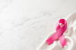 © warleysoares - Laço de cetim rosa sobre fundo de mármore branco com amplo espaço para texto - Conceito de conscientização sobre o câncer de mama, cuidado e prevenção.