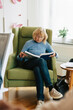 © Maskot - Elderly woman reading book while sitting in armchair at retirement home