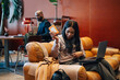 © Maskot - Female entrepreneur connecting external hard drive to her laptop while sitting on leather sofa at coworking space