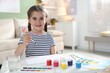 © New Africa - Little girl drawing picture with paints and brush at white desk indoors, space for text