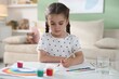 © New Africa - Little girl drawing picture with paints and brush at white desk indoors