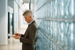© Maskot - Side view of senior businessman analyzing reports while leaning on glass brick wall