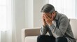 © Ariestia - Depressed Senior Asian Man Sitting on Sofa Covering Face with Hands Feeling Sad and Stressed at Home