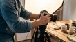 © Nova_Genera_Stock - Photographer adjusting professional camera on tripod during product photo shoot of handmade ceramic mugs