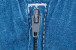 © Alexander Piragis - Closed metal zipper on blue denim fabric. Close up of jeans fly fastener. Textile texture and clothing detail for fashion design. Background for garment manufacturing industrial sector
