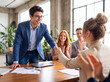 © Three-Studio - Professional young businessman shaking hands with a female colleague, celebrating success in a modern office meeting.