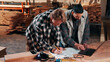© peopleimages.com - Men, laptop and documents in lumber workshop, carpenter and team with invoice, writing and woodwork. Conversation, collaboration and people with tech, notes and online order with carpentry planning