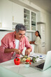 © Marko Geber - Middle-aged man chopping vegetables while following an online recipe in a home kitchen