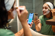 © Marko Geber - Young woman applying facial mask while texting in bathroom