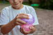 © Татьяна Швец - Smiling little boy playing with a glittery dumpling shaped squishy toy outdoors, squeezing a colorful sensory stress relief toy during fun playtime in the garden