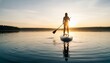 © ANDREY PROFOTO - Woman paddleboarding on calm lake at sunset