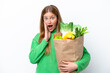 © luismolinero - Young caucasian woman holding a grocery shopping bag isolated on white background with surprise and shocked facial expression