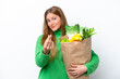 © luismolinero - Young caucasian woman holding a grocery shopping bag isolated on white background making money gesture