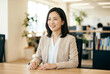 © TMGM - オフィスの会議室で笑顔で座るベージュのジャケットを着た30代日本人女性