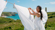 © Маргарита Пархоменко - Woman hanging laundry on a clothesline with a scenic coastal view