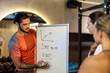 © Mediteraneo - Two athletic women listening to a personal trainer writing a fitness program on a whiteboard.