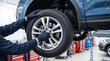 © Taras Roshchuk - A person works on a vehicle inside an auto repair shop. They are using tools to take off a tire. The scene shows equipment and other cars in the background
