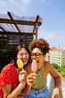 © BONNINSTUDIO/Stocksy - Friends enjoying refreshing fruit popsicles on sunny rooftop