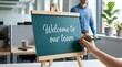 © Stocker - Welcome to our team message on blackboard easel with hand holding pencil office background welcoming new employee joining company business concept.