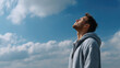 © syhin_stas - Young man taking a deep breath and closing eyes, finding relaxation and inner peace under open clear blue sky with soft white clouds, embracing freedom, mindfulness