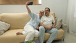 © ADDICTIVE STOCK - Senior couple taking a selfie together on living room sofa