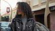 © Krakenimages.com - Teenage woman with curly hair smiles and looks left wearing a black puffer jacket on a city street near parked cars; carefree joy.