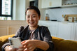 © Davor - Smiling woman using smartphone at home in modern kitchen