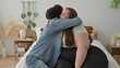 © Krakenimages.com - Woman in striped tee sits on bed holding man's hand and leaning in for a hug, smiling warmly amid pillows and decor in a building; intimacy support warmth.