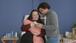 © Krakenimages.com - Woman cradling swaddled baby while partner checks smartphone in a nursery building and smiles at the screen; family bond tenderness.