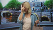 © Krakenimages.com - Young blonde woman holding shopping bag, pinching bridge of nose with hand to face in street by canal and bridge lights; frustration errand.