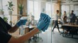 © Varos - A janitor wearing blue nitrile gloves cleaning a glass office partition with a spray bottle and a cloth, with colleagues working in the blurred background.