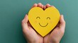 © oksa_studio - Hands cradling a yellow heart with a smile to show love care kindness and support