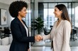 © mila103 - Two women shake hands in a modern office space. They smile warmly, showing mutual respect and collaboration. The setting features large windows and minimalist decor