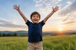 © mila103 - Child beams joyfully with arms wide open. Sunset paints golden sky above green field. Mountains fade softly in background distance. Open air feels free and peaceful. Perfect for themes of joy, nature