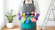 ©  AH Creation - Professional cleaner person holding a blue bucket filled with cleaning supplies and colorful cloths in a bright room