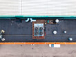 © AmazingAerialAgency - Aerial view of industrial rooftop featuring HVAC cooling units, ventilation pipes, and a white van parked below in Riga, Latvia.