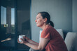 © Bits and Splits - Middle-aged woman sits on a balcony holding a coffee cup and gazes thoughtfully into the distance. Quiet, reflective morning moment.