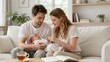 © mihrzn - A young couple sits together on a beige couch, gently cradling and adoring their awake newborn baby in a bright, cozy home setting.