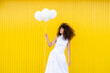 © VISTA by Westend61 - Woman in white dress holds white balloon against yellow background
