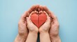 © A.K .Studio - Close up of an adult pair of hands gently holding a small child pair of hands containing a bright red folded paper heart on blue background.