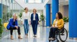 © agus - Three women in business attire walking and sitting in an office lobby with a woman in a wheelchair