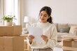 © Vasiliy - Young woman reading a lease agreement in her new home. Happy female tenant with moving boxes in a bright apartment. Relocation and real estate concept