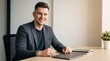 © Eve - Smiling caucasian businessman in grey blazer sitting at office desk with laptop. Confident handsome male entrepreneur or creative manager working in bright modern workspace environment.