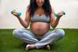 © ADDICTIVE STOCK - Pregnant woman exercising with dumbbells on grass outdoors