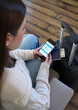 © Will Labrador - Mujer realizando check-in online desde su teléfono móvil junto a su equipaje, pasaporte y dinero de viaje