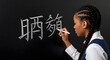 © Rusdan - Young African American student writing Chinese characters on a blackboard in a classroom.